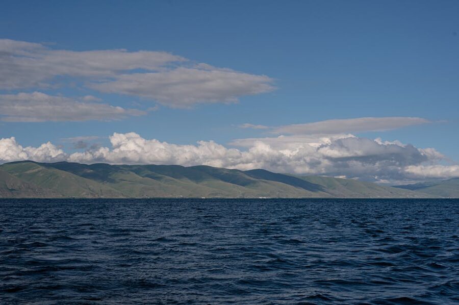 Lake Sevan with green hills and fluffy clouds under a blue sky